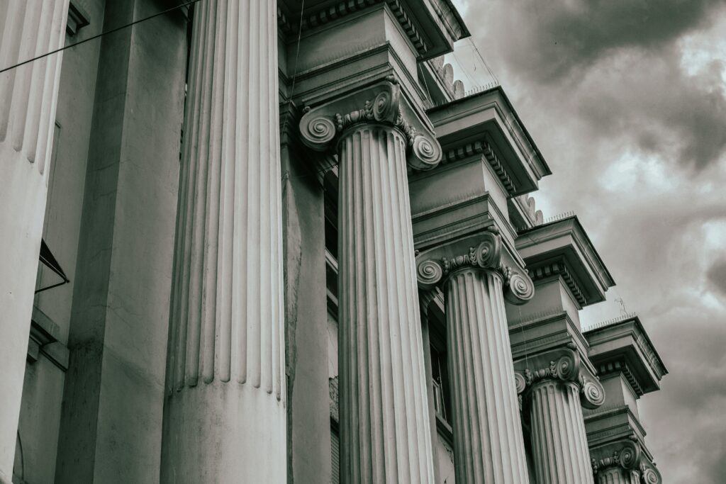 pexels-photo-18746178-18746178 Dramatic grayscale image of Greco-Roman columns against a cloudy sky.