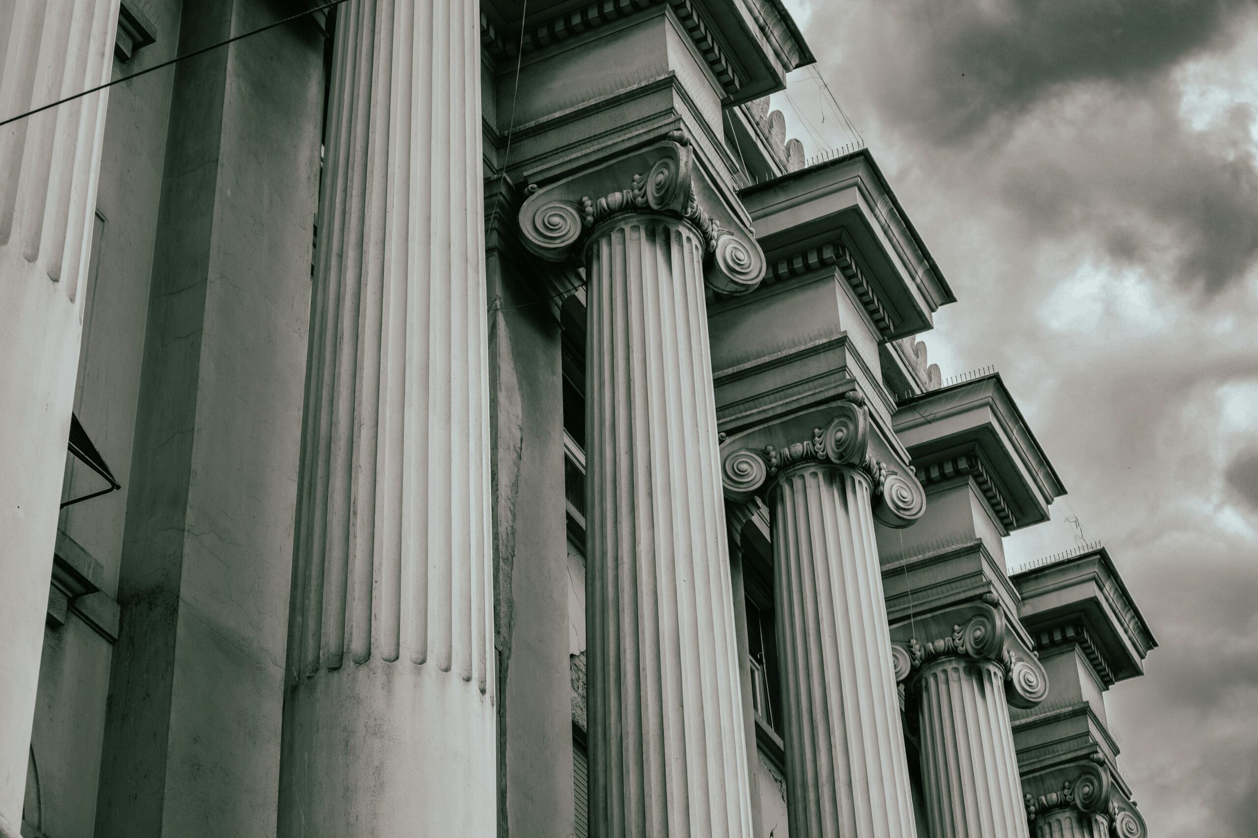 Dramatic grayscale image of Greco-Roman columns against a cloudy sky.